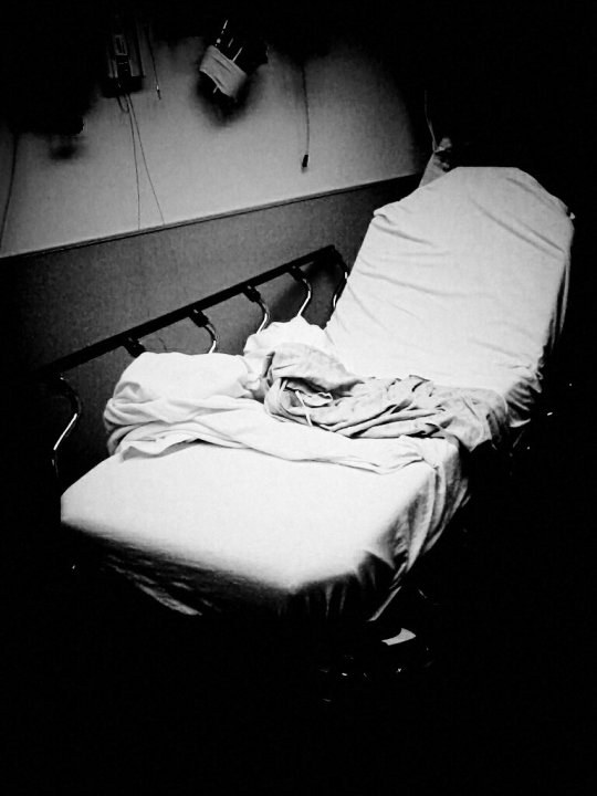 Black and white photo of emergency room bed with messy sheets.