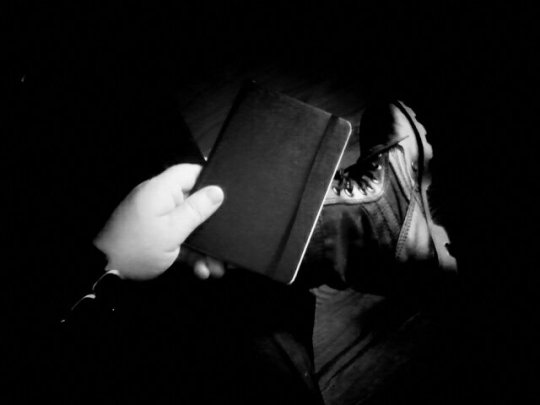 Black and white photo of hand holding sketchbook. Resting sketchbook on jungle boot.