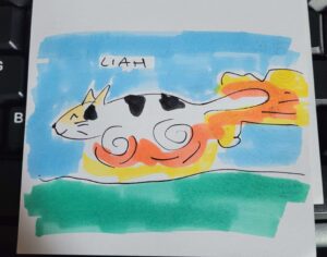 Photograph of a marker drawing of Liah the cat. Her legs are spirals and there are flames coming off of her tail because she is like a rocket with legs. The sky behind the cat is light blue, the ground is green.