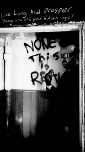 Black and white photo of stairwell with graffiti on the walls. The message written is "None of this is real."