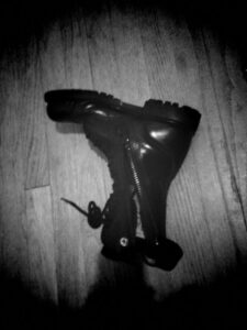 Black and white photograph of one unzipped leather military paratrooper jump boot laying on it's side on a wood floor.