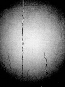 Black and white photo of close up of cracks on a dirty white wall.