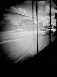 Black and white photo of a street with cars reflected onto a dirty storefront window.