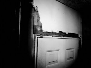 Black and white photo of destroyed wall and door.