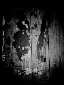 Black and white photo of wood floor with wear, glue, and paint splotches.