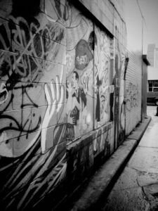 Black and white photo of alley with wall covered in graffiti art.