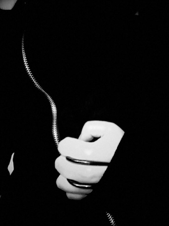 Black and white photo of hand wearing two hook rings. Hand is in front of zipper on a black jacket.