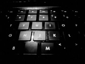 Black and white close up photo of letters on center of black keyboard.