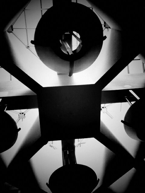 Black and white photo of lighting fixture on ceiling of mall/shopping center.