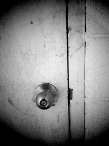Black and white photo of door handle with lock on the knob. The door is very dirty.