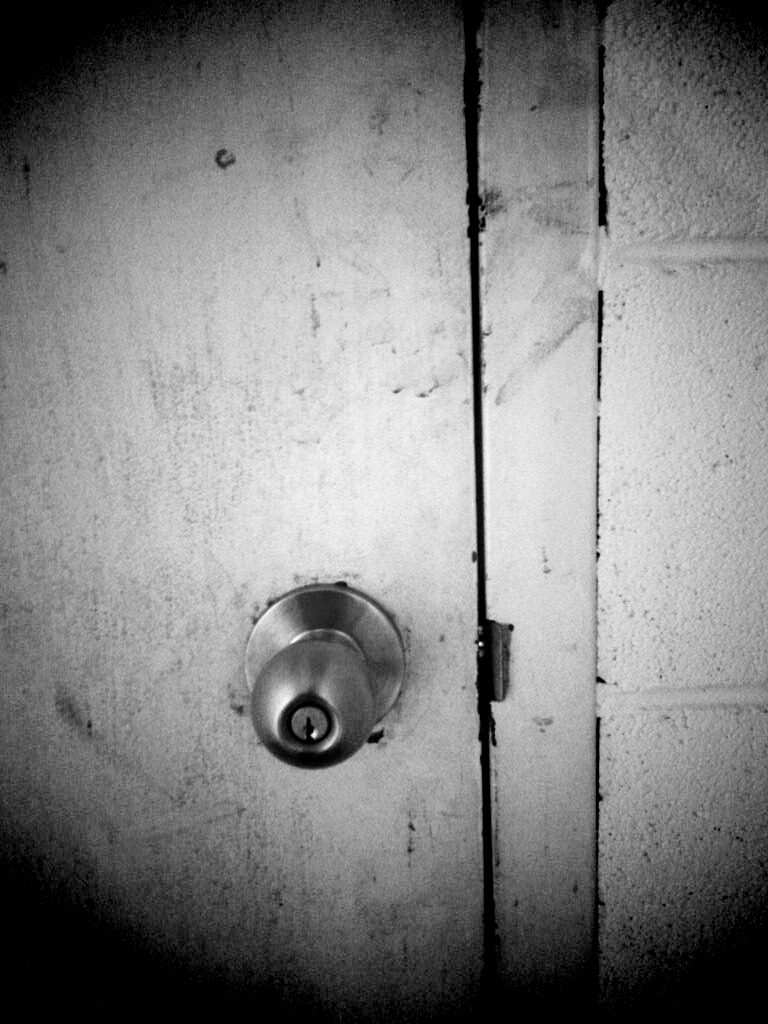 Black and white photo of door handle with lock on the knob. The door is very dirty.