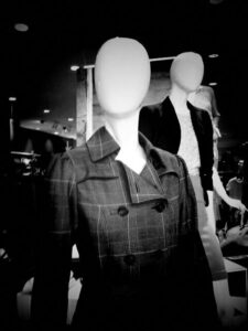 Black and white photo of two mannequins in a department store. The mannequins have blank faces.