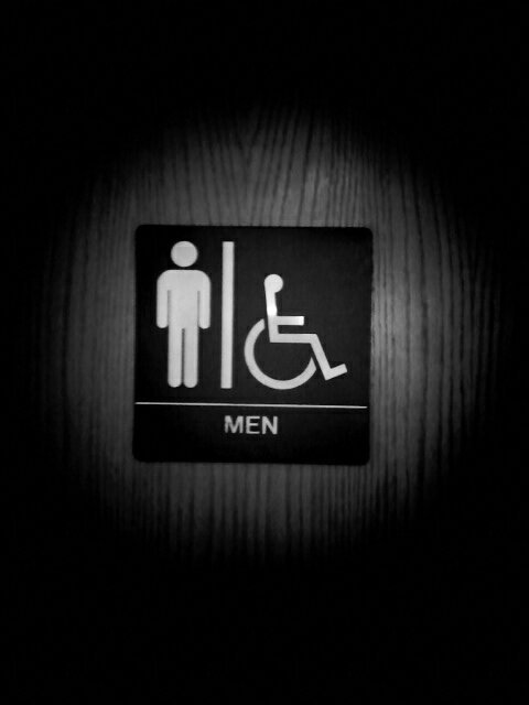 Black and white photo of men's room/restroom sign on wood door.