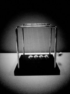 Black and white photo of swinging Newton's cradle on a table.