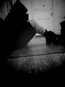 Black and white photo/self portrait of reflection of myself sitting on dirty wood floor in room with white walls