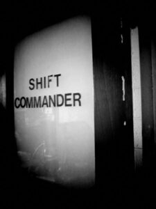 Black and white photo of door. Glass on door has the words shift commander