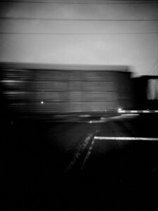 Black and white photo of blurry train going across road crossing.