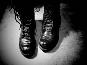 Black and white photo of two very worn leather combat jump boots. The boots are untied.