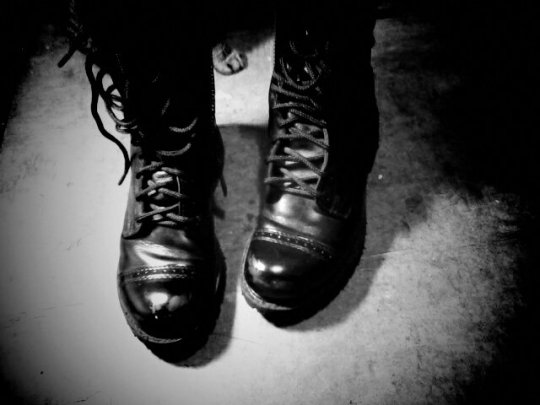 Black and white photo of two very worn leather combat jump boots. The boots are untied.