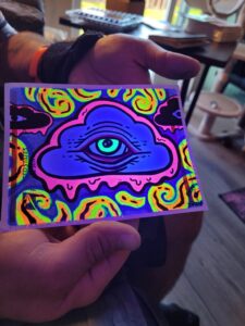 Photo of marker art on a sticker depicting a cloud with an eye dripping ooze under UV black light.