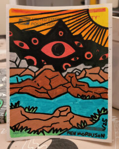 Photo of marker art on sticker. Art depicts a black mountain with eyes of varying sizes inside, then rocky terrain in front of it. The sun is off to the right, shining it's rays. This is the work in progress photo.